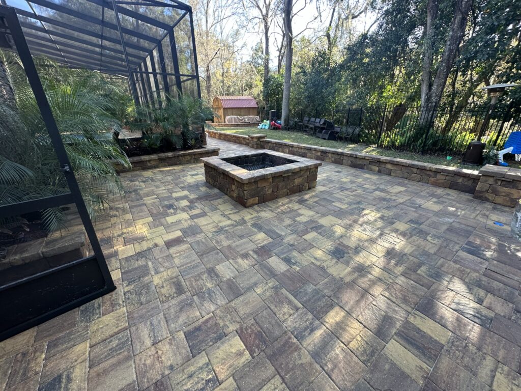 A spacious outdoor patio with a stone fire pit, surrounded by greenery and a screened enclosure.